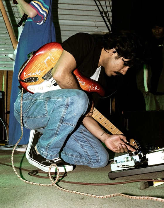 A young man with a guitar bends over his sound pedals wearing black and white Skate Authentic.