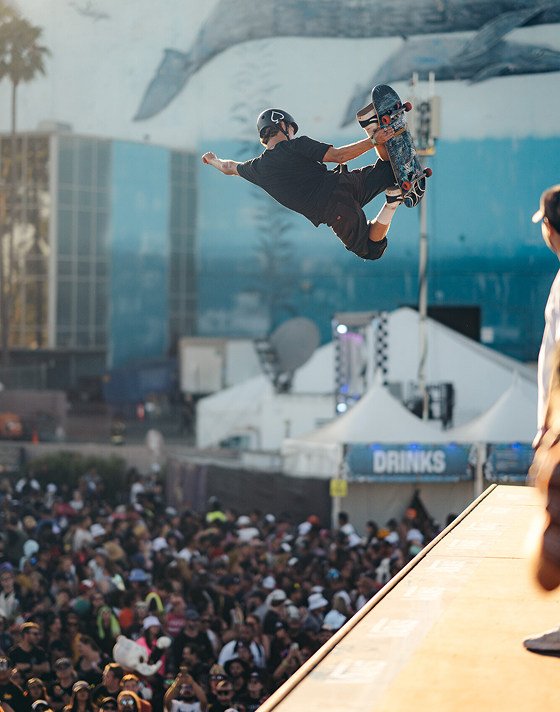 A skater gets air on a halfpipe and does a Stalefish grab as the crowd watches at Vans Warped Tour.