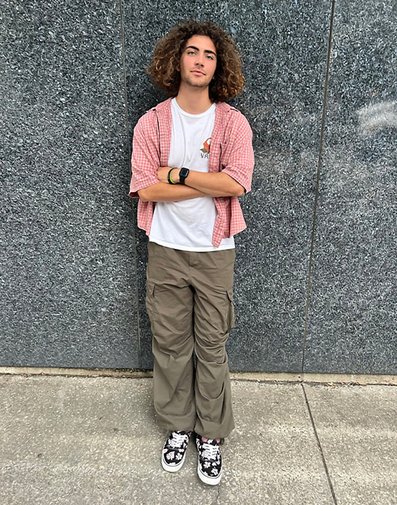 A young man leans against a wall wearing black and pink palm print Authentic.
