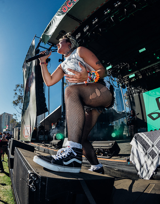 A young woman singing at the crowd on-stage wearing black and white Sk8-Hi at Vans Warped Tour.