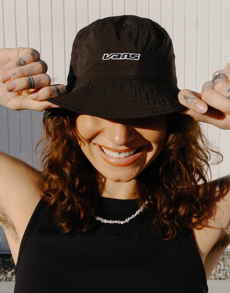 Close-up on a young woman smiling in the sun wearing a faded black Dropped V Bucket Hat.