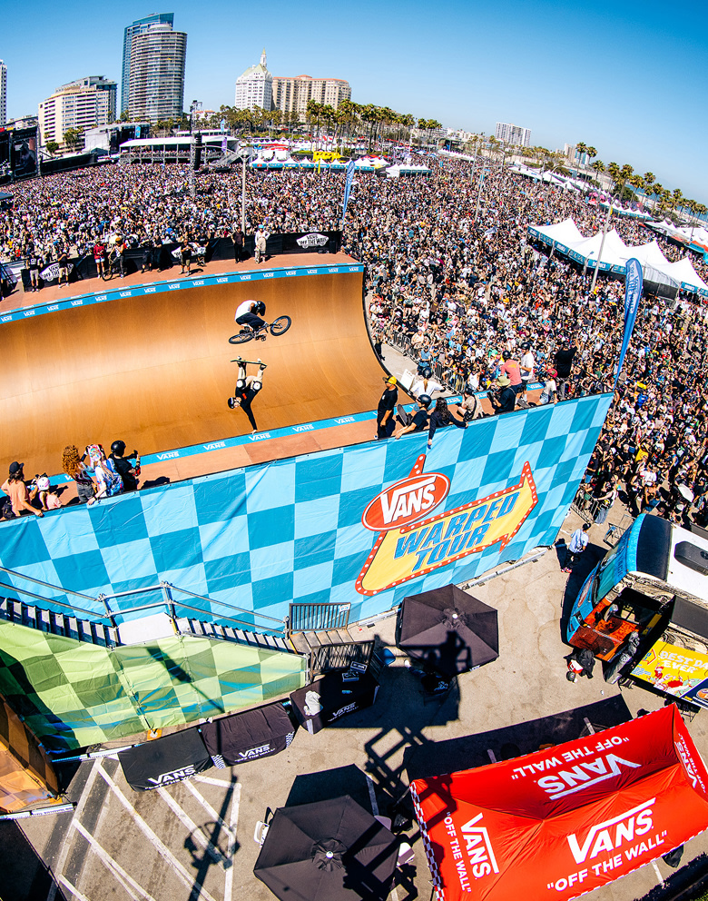 An overhead shot of a BMX rider and a skater in a half pipe surrounded by a crowd at Vans Warped Tour.