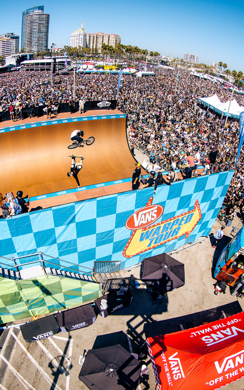 An overhead shot of a BMX rider and a skater in a half pipe surrounded by a crowd at Vans Warped Tour.