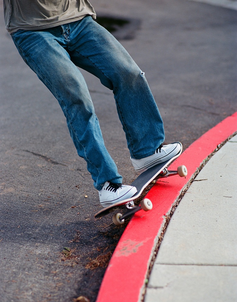 Split image. Left, medium shot of a skater grinding a red cement curb outside wearing white Vans. Right, white and green Vans mounted on a wall.