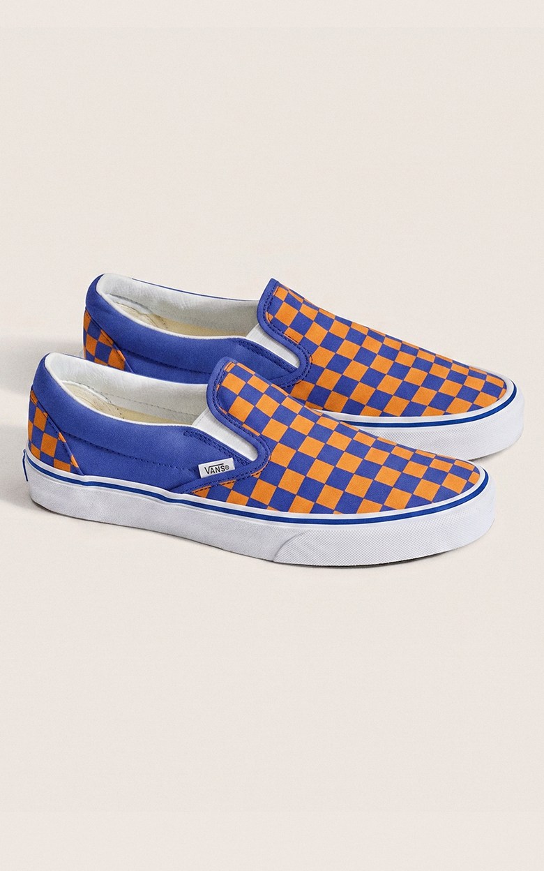 A pair of orange and blue Checkerboard Classic Slip-On on the floor of a photography studio.