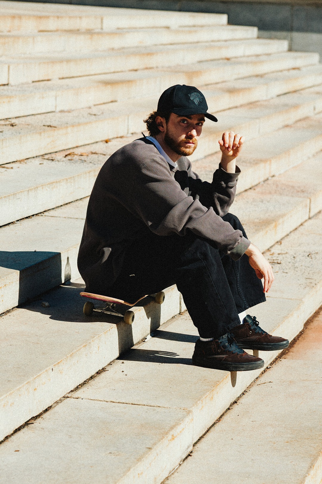 Image of a skateboarder sitting on his skateboard on a staircase.