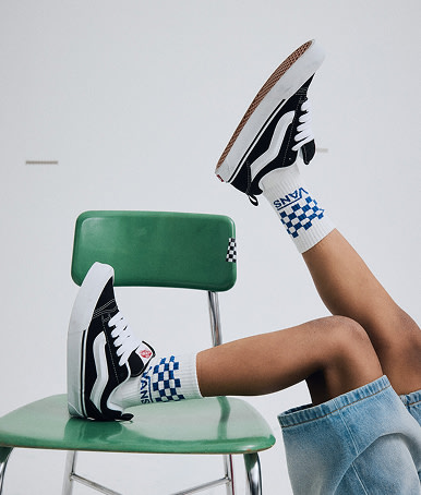 Close-up on a young boy wearing black and white Knu Skool with blue Kids Classic Check Crew Socks on a classroom chair.