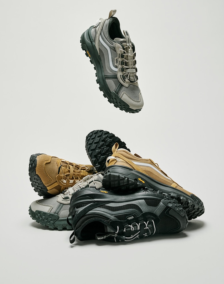 Various pairs of the Crosspath XC in the oatmeal colorway, the autumn brown colorway, and the black and gray colorway in a pile in a photo studio.