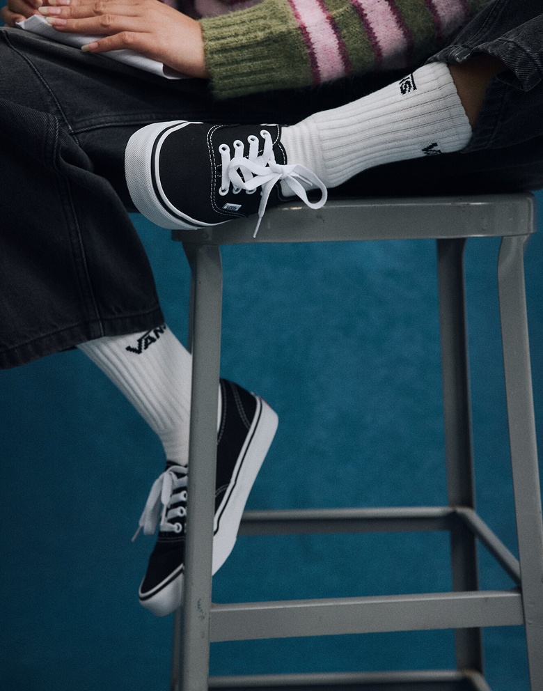 Close-up on a young woman wearing black and white Authentic with white Vans crew socks on a metal stool.