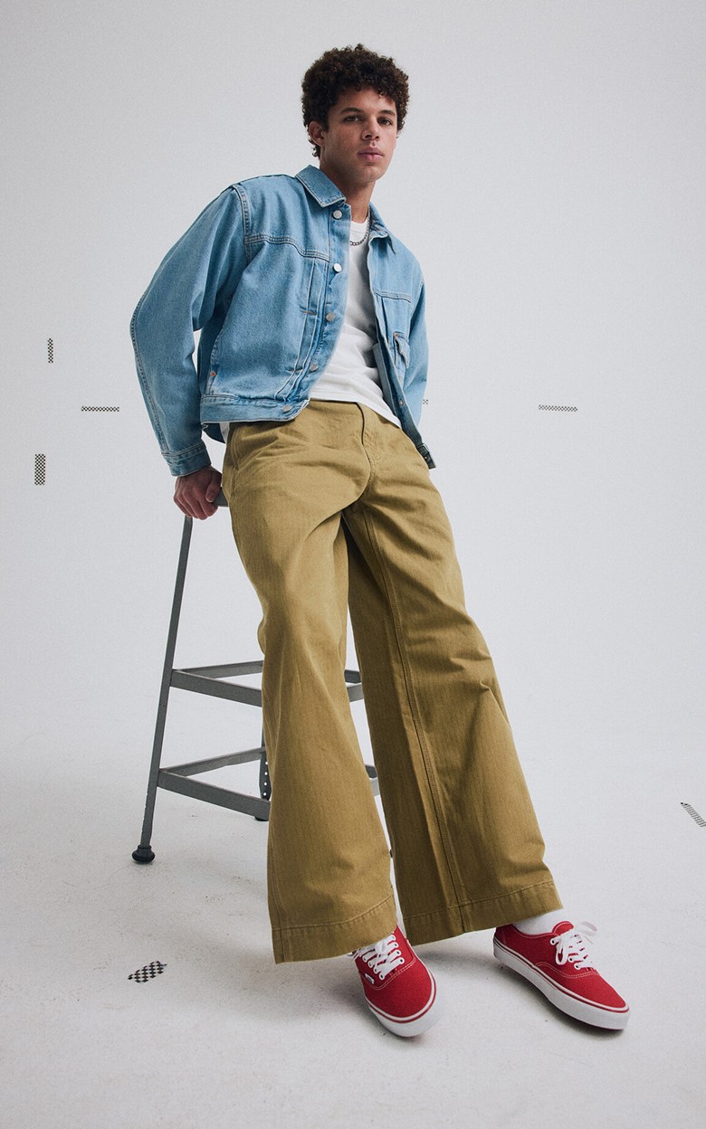 A young man wearing red Authentic, a blue Check-5 Denim Trucker Jacket, and brown Authentic Chino Loose Pants in a photography studio.