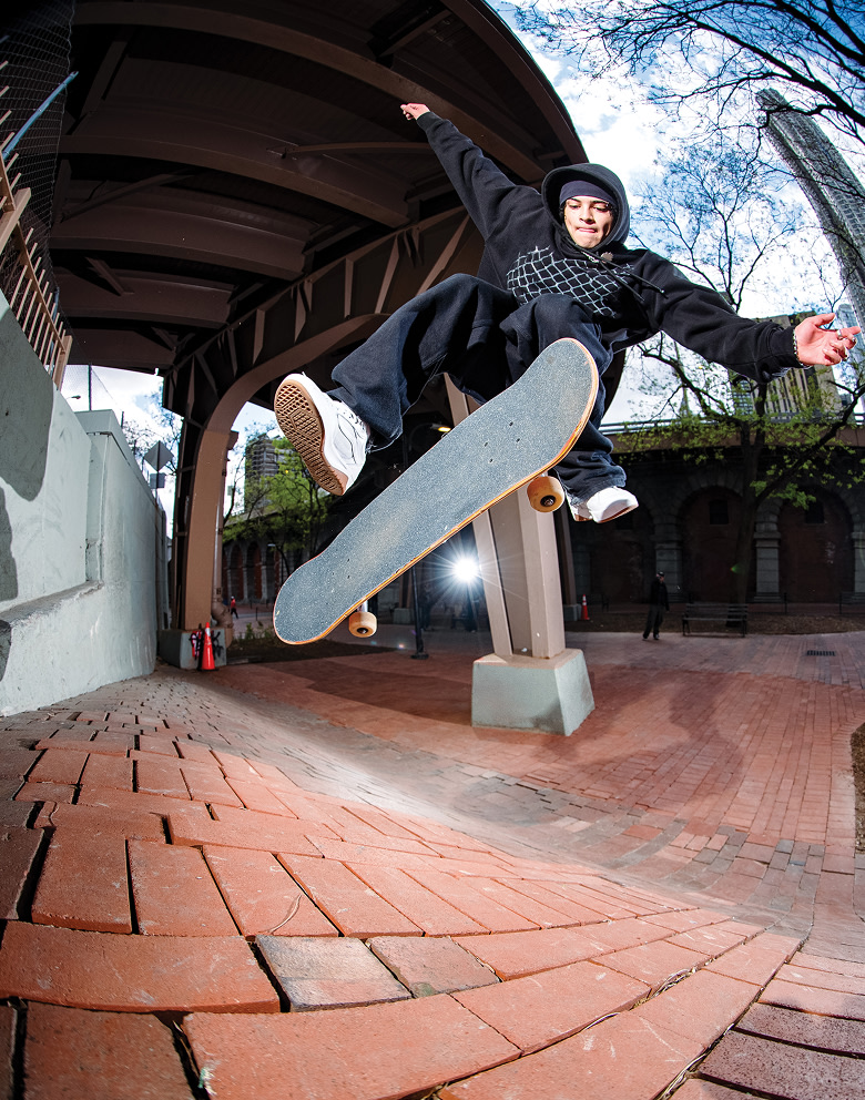 An image of a skater in mid-air doing a flip trick off a brick rise under a freeway wearing Vans shoes and clothes.