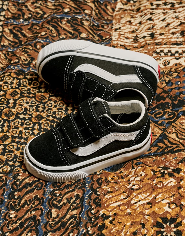 Close-up on a pair of black and white Little Kids Old Skool V shoes on a patterned couch.
