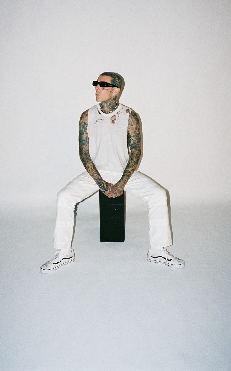 Blink-182 drummer Travis Barker sits in a photography studio wearing the white Vans X Travis Barker Old Skool.