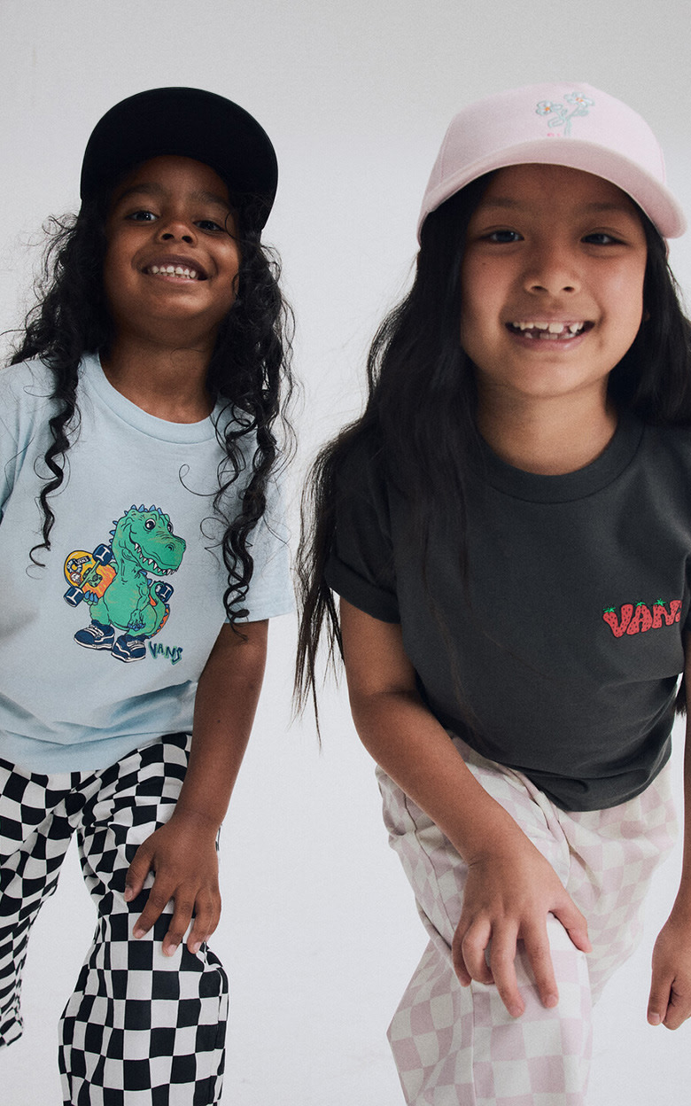 A young boy and girl lean in and smile at the camera wearing Vans clothes and hats.