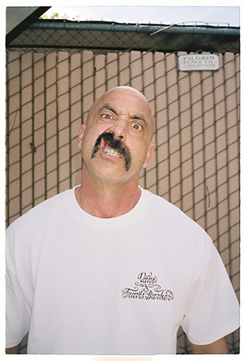 Image of a man staring into the camera wearing a white tshirt.