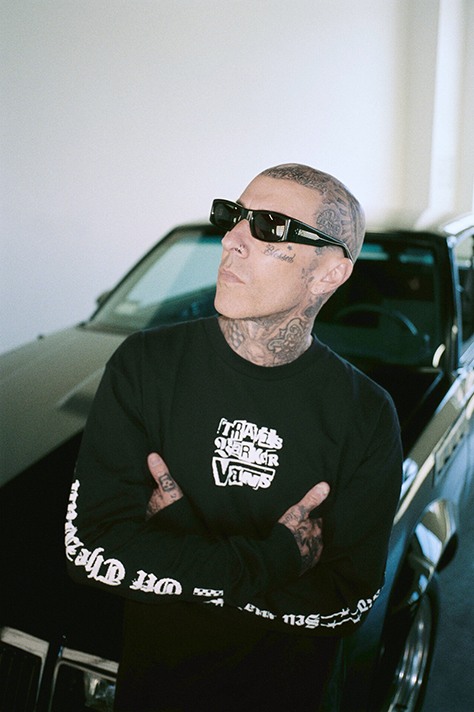 Image of Travis Barker in a car garage with a car behind him.