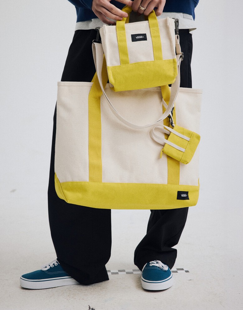 Waist down medium shot of someone holding three different sizes of yellow and white Pergs totes and bags.