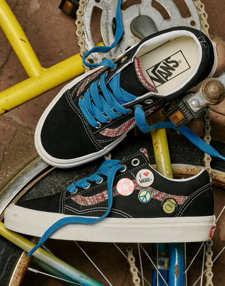 An overhead shot of a black and white Big Kids Old Skool Shoe with Vans buttons and blue laces on a brick sidewalk.