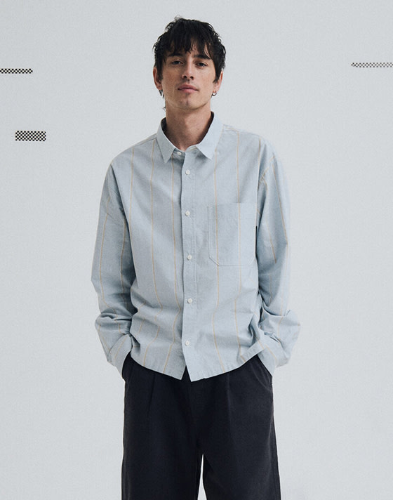 A young man poses in a photography studio wearing a Lawson Solid Oxford Long Sleeve Shirt.