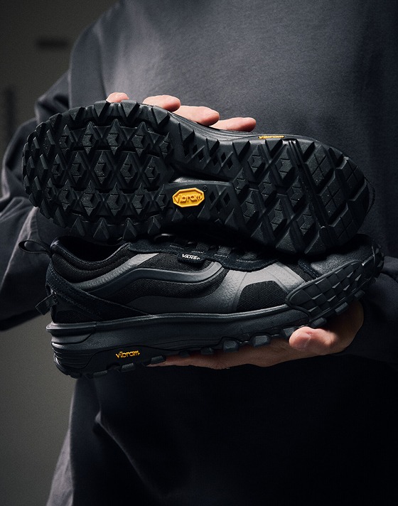 Close-up on a young man holding a pair of black Ultrarange 2.0 shoes showing the tread of the Vibram sole.