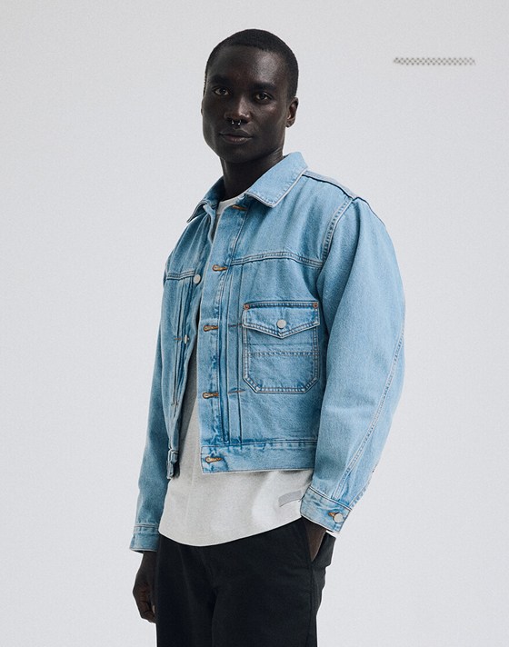 A young man poses in a photography studio wearing a light stonewash Check-5 Denim Trucker Jacket.