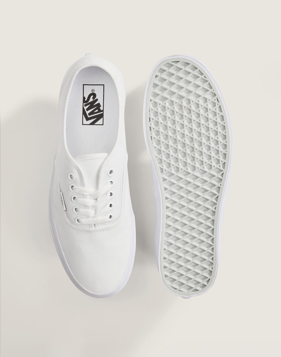 An overhead shot of a pair of white beige Authentic shoes on the floor of a photography studio.