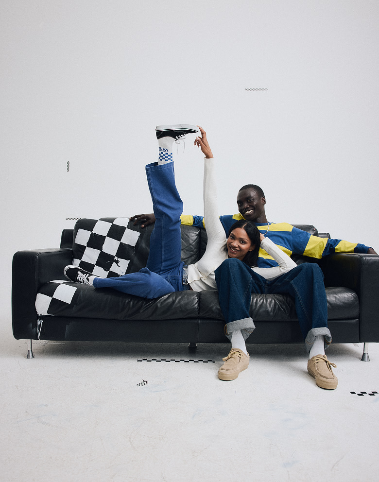A young man and woman lie on a couch together wearing Vans shoes and clothes in a a photography studio.