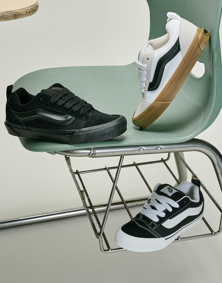 An all-black Knu Skool, a white and gum Knu Skool, and a black and white Knu Skool laid out on and around a school desk.