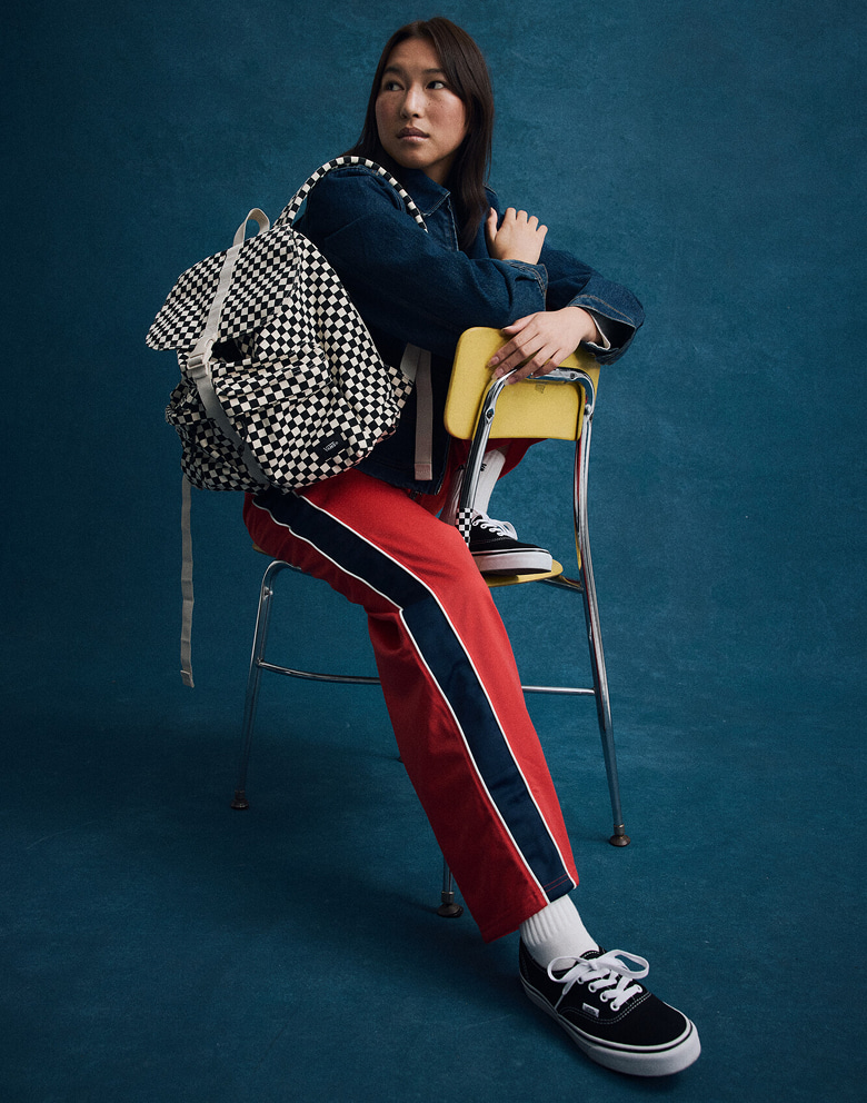 A young man poses against a picture day background wearing Vans shoes, clothes, and a backpack.