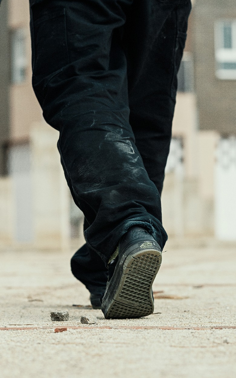 Close-up on a young man walking away on the concrete in black Old Skool with the Vans logo visible.