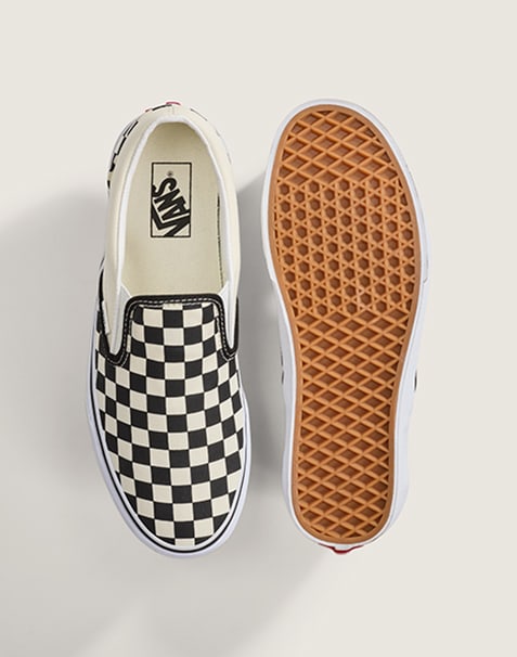 An overhead shot of a pair of black and white Classic Slip-On Checkerboard Shoe on the floor of a photography studio.
