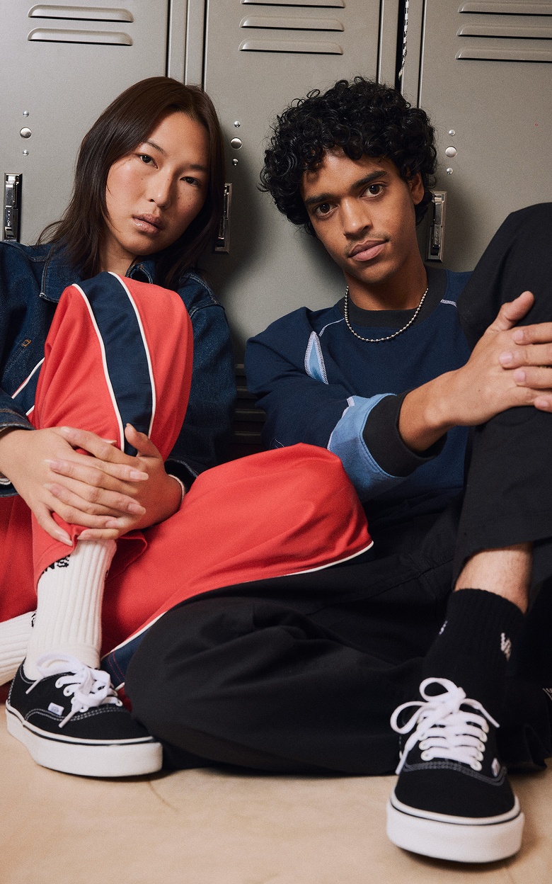 A young man and woman lean up against school lockers wearing Vans shoes and clothes.