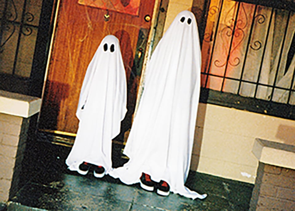 Two sheet ghosts and two people wearing vans apparel and footwear on a porch.