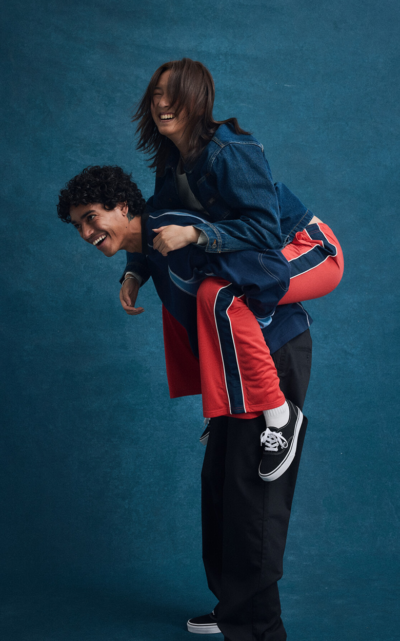 Blue school picture day backdrop. A woman is on a man’s shoulders and they’re both smiling and laughing. They’re both decked out head to toe in Vans.