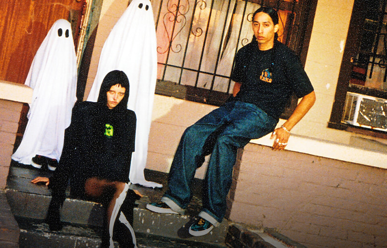 Two people wearing Vans apparel and sneakers sitting outside a house with ghoss in the background.