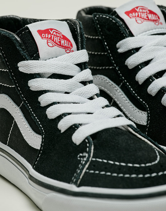 Close-up on a pair of black and white Sk8-Hi on the floor of a photography studio.