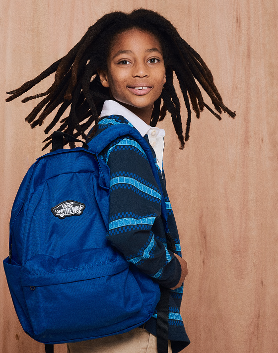 Medium waist up action shot of a kid turning their head while wearing a blue Kids V Rugby Long Sleeve and a blue Old Skool Grom Backpack.