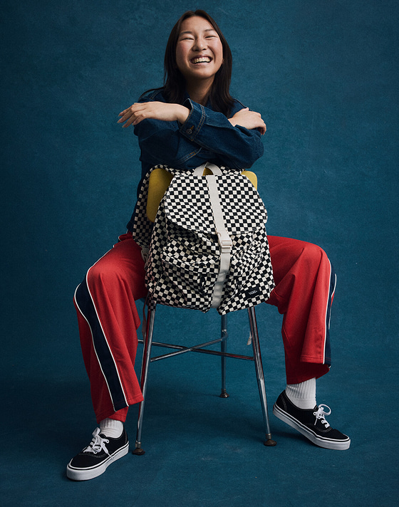 Medium full body shot of a woman wearing a denim jacket, track pants, the black and white Authentic, and the Scatter Backpack in checkerboard.