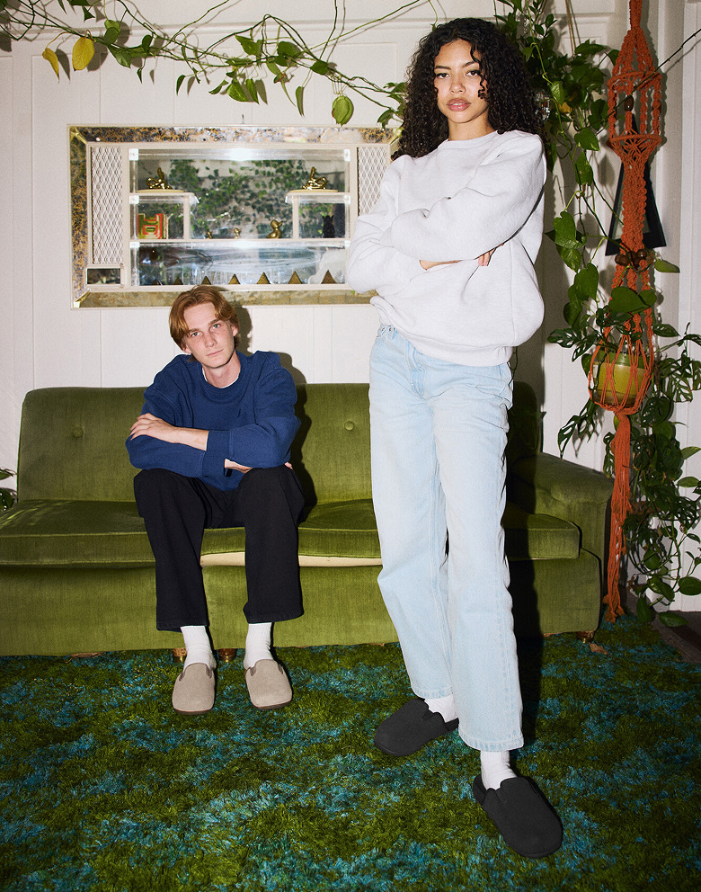 Medium shot of a man in a woman in a green retro living room. She’s wearing the Harbor Mule VR3 in black. He’s wearing the Harbor Mule VR3 in khaki.