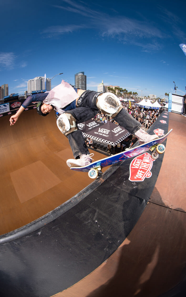 Wide fish eye shot of Lizzie Armanto wearing the Skate Lizzie in Pale Petal Pink skating the top of a half pipe in front of a huge crowd.