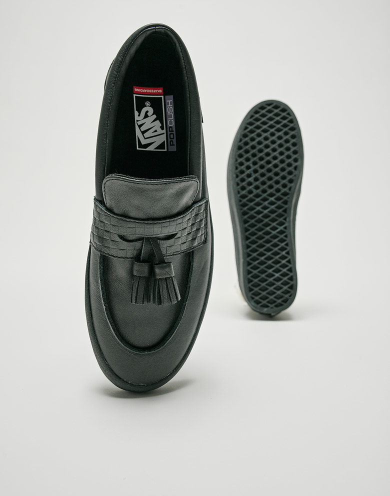 A black pair and a brown pair of Skate Loafer Tassel shoes lie on the floor in a photo studio.