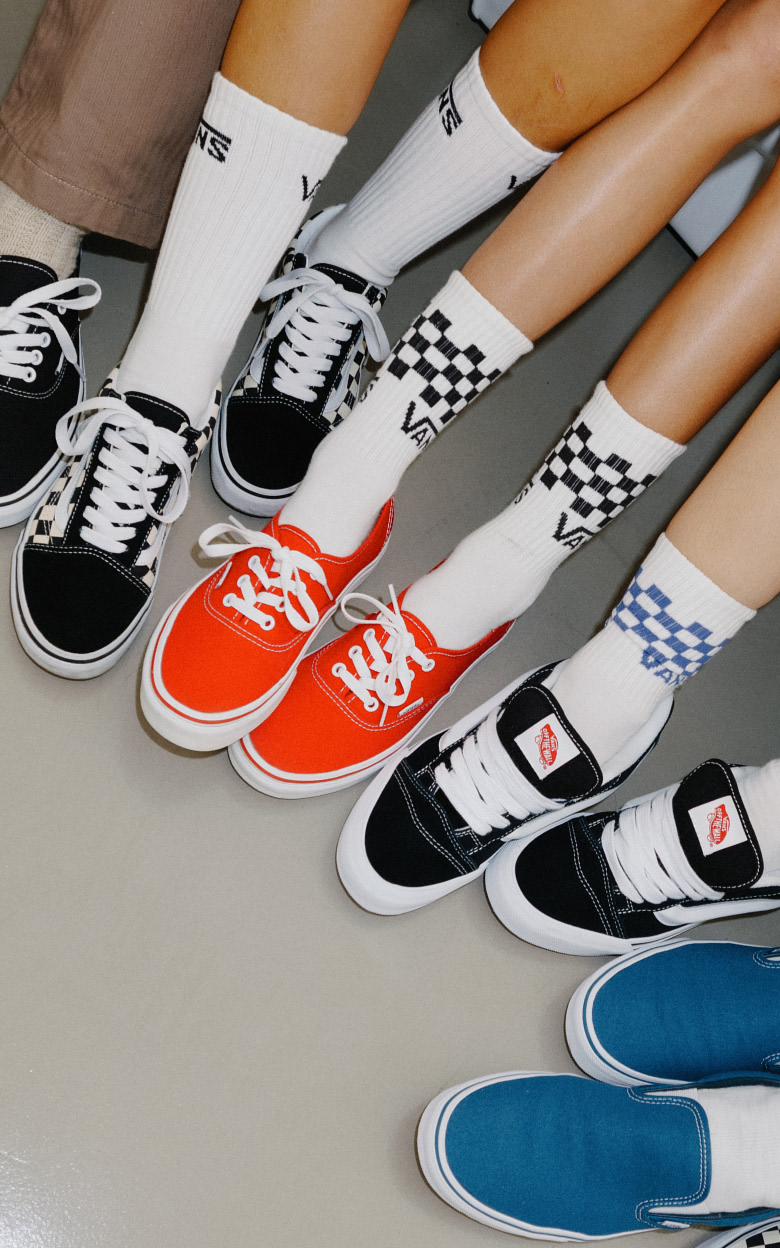A bunch of black and white Vans Icons on the floor of a photo studio including the Authentic, Checkerboard Classic Slip-On, Knu Skool, and more.