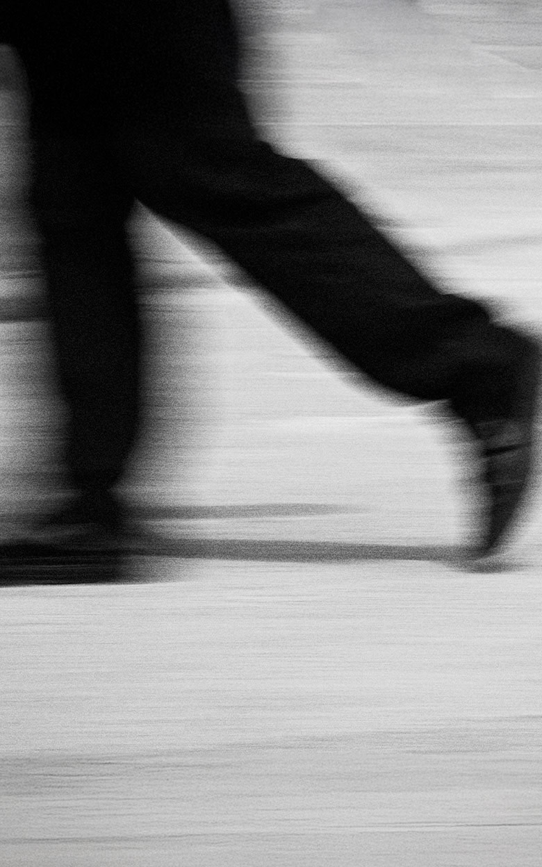 A blurry black and white photo of a skater walking in Vans shoes on the concrete.