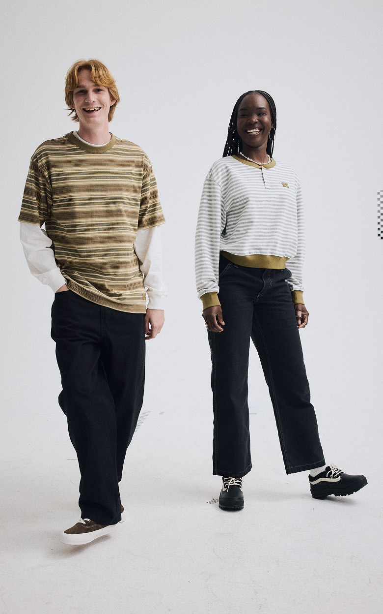 Wide shot of a man and a woman in a gray photography studio. Both of them are smiling and dressed head-to toe in Vans.