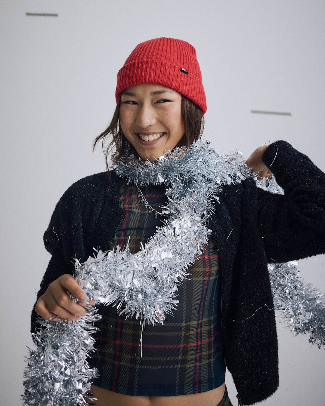 Person wearing a red beanie, plaid top, and black cardigan wrapped in silver holiday tinsel. Gifts for Her.