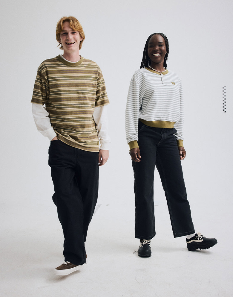 Wide shot of a man and a woman in a gray photography studio. Both of them are smiling and dressed head-to toe in Vans.