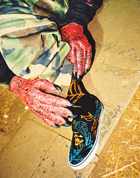Close up knee down shot of someone wearing red ghoul hands and a pair of the Classic Slip-On Shoe in Glow-in-the-Dark Black / Citrus Burst Orange.