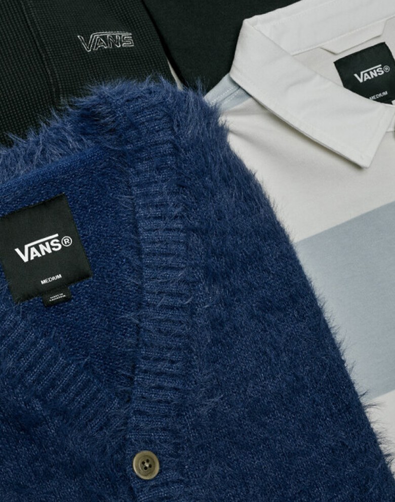 Close up flat lay shot of multiple cold-weather tops on the floor of a grey photography studio.