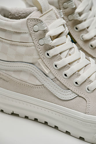 Close-up of a light-colored Vans high-top shoe with white laces and suede detailing.