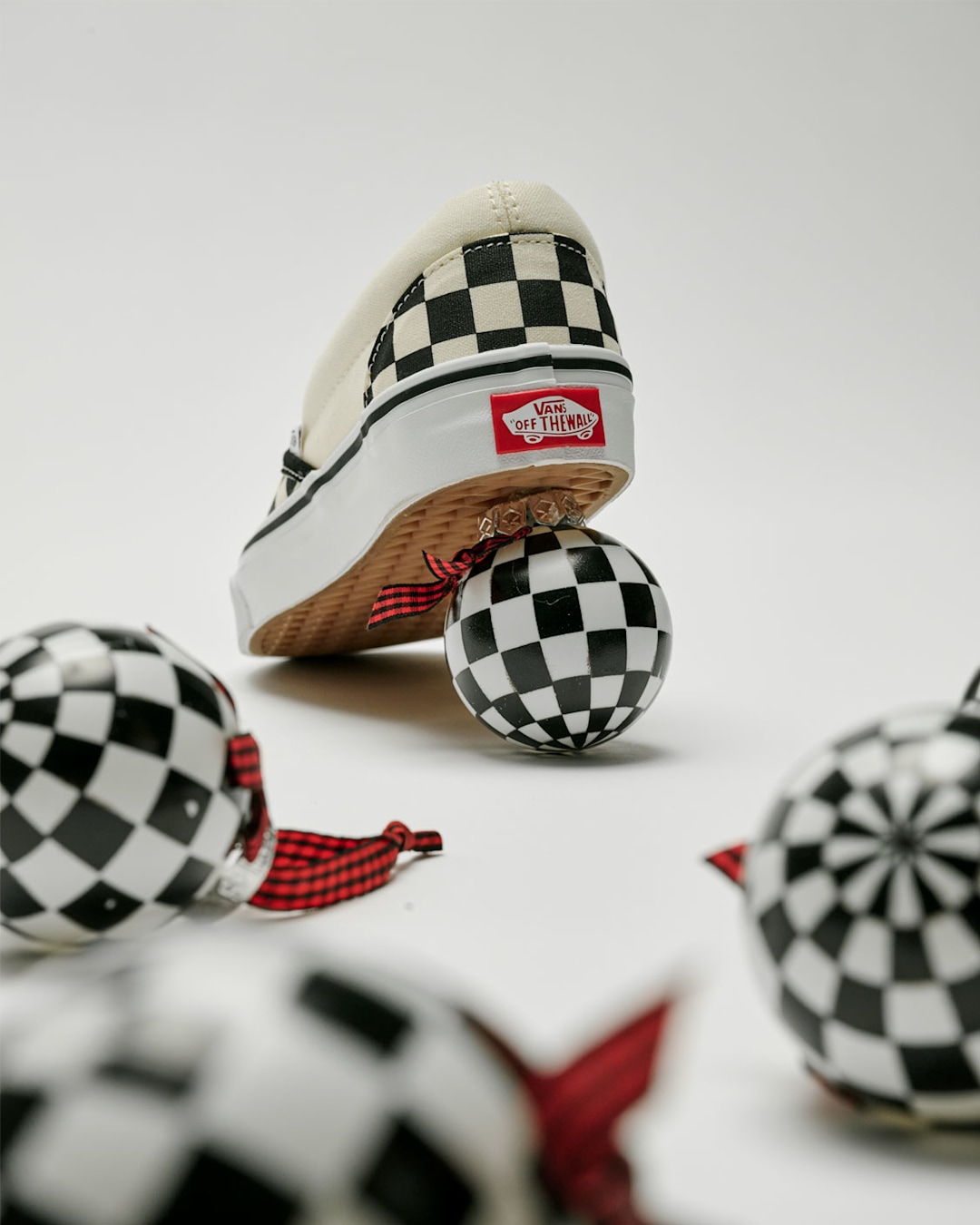 White Vans checkerboard shoe displayed with black-and-white checkerboard ornaments on a light background. Text reads 'Checkerboard"